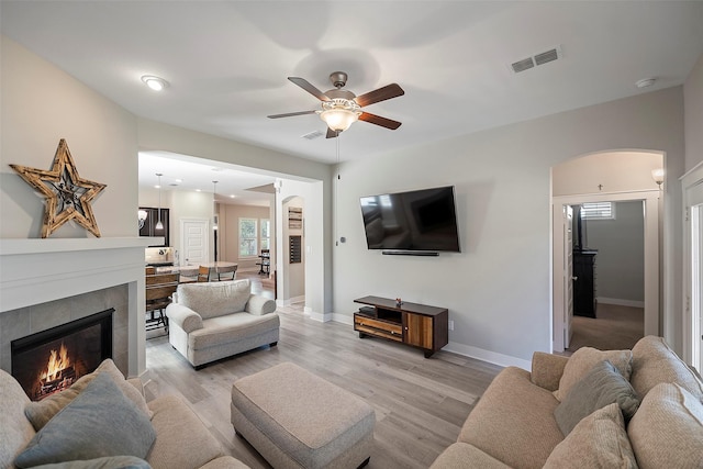 living room featuring arched walkways, a tiled fireplace, visible vents, and light wood-style floors