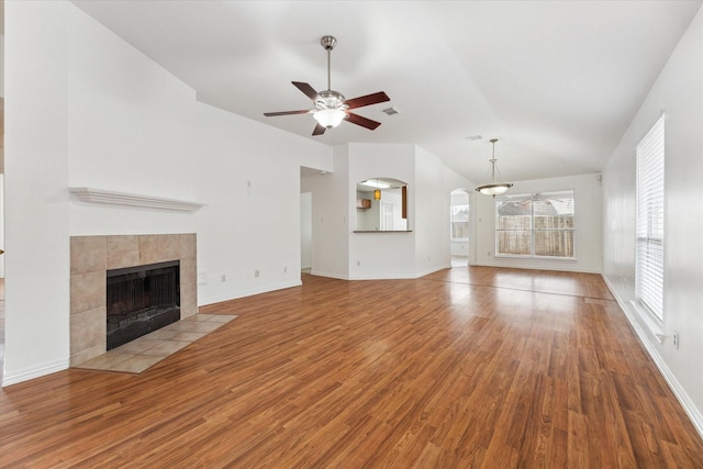 unfurnished living room featuring baseboards, a tiled fireplace, lofted ceiling, ceiling fan, and wood finished floors