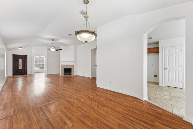 unfurnished living room with arched walkways, vaulted ceiling, light wood-type flooring, and a tile fireplace