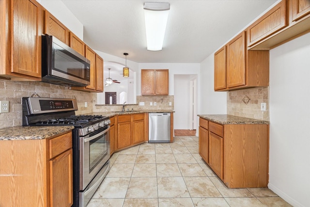 kitchen featuring brown cabinetry, appliances with stainless steel finishes, light stone counters, and a sink