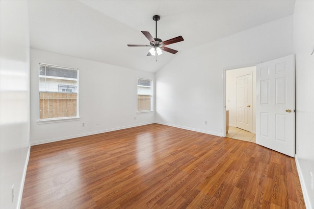 empty room featuring lofted ceiling, light wood-style flooring, baseboards, and a ceiling fan