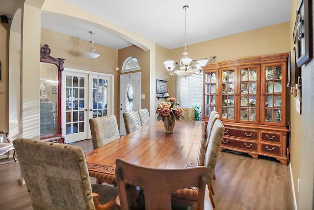 dining space featuring arched walkways, french doors, a notable chandelier, and wood finished floors