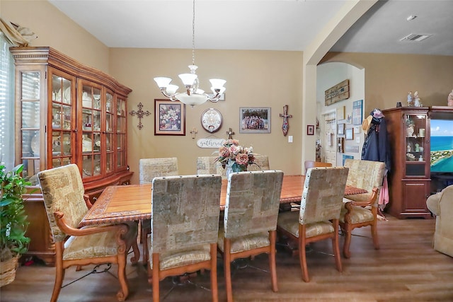 dining area with arched walkways, wood finished floors, a chandelier, and visible vents