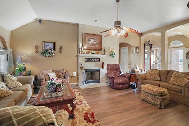 living room featuring arched walkways, a ceiling fan, wood finished floors, vaulted ceiling, and a fireplace