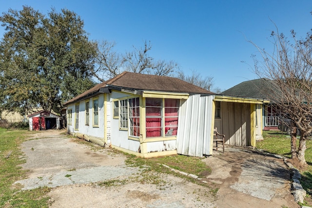 exterior space with driveway, a shingled roof, and an outbuilding