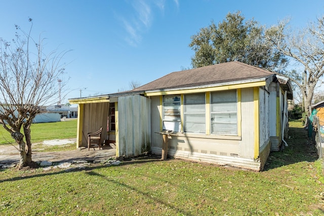 rear view of property with a shingled roof and a lawn