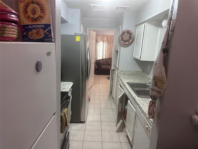 kitchen featuring light tile patterned floors, visible vents, white cabinets, a sink, and range