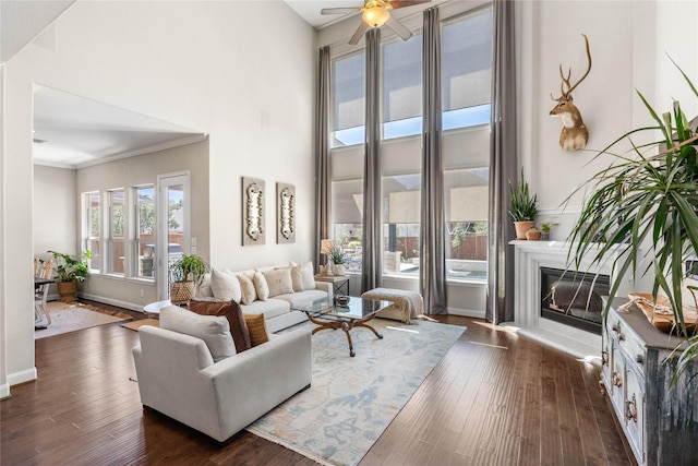 139 Ballantyne Dr, Montgomery, TX 77316 - living area featuring baseboards, a glass covered fireplace, a ceiling fan, dark wood-type flooring, and a high ceiling