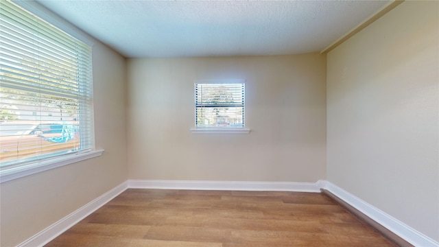 empty room featuring light wood-style floors, baseboards, and a textured ceiling