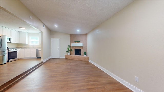 unfurnished living room with a textured ceiling, a large fireplace, visible vents, baseboards, and light wood-style floors