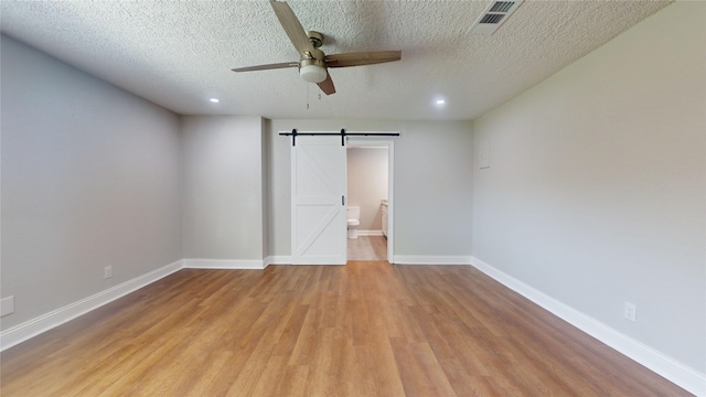 unfurnished bedroom featuring visible vents, light wood-style flooring, a barn door, a textured ceiling, and baseboards