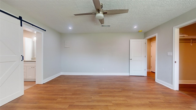 unfurnished bedroom featuring a barn door, light wood-style flooring, visible vents, and baseboards