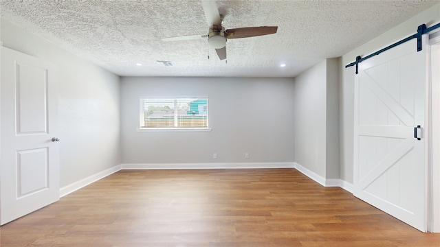 spare room featuring a barn door, visible vents, baseboards, a ceiling fan, and light wood finished floors