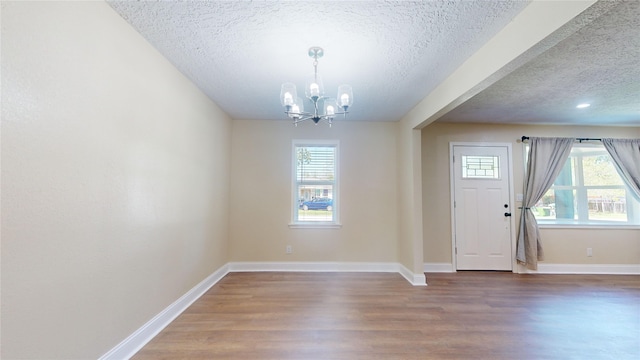 foyer entrance featuring baseboards, a textured ceiling, wood finished floors, and a notable chandelier