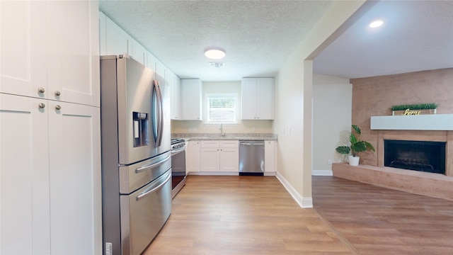 kitchen with stainless steel appliances, a fireplace, a sink, open floor plan, and light wood-type flooring