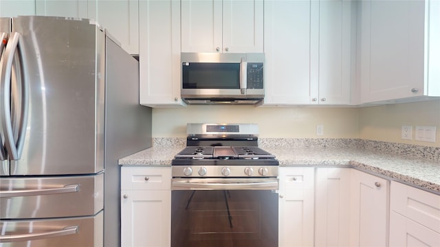 kitchen with stainless steel appliances, light stone counters, and white cabinetry