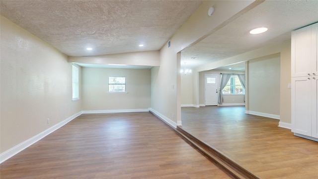 empty room with a textured ceiling, a healthy amount of sunlight, wood finished floors, and baseboards