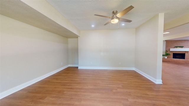 spare room with light wood finished floors, baseboards, a fireplace with raised hearth, and a textured ceiling