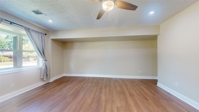 spare room with a textured ceiling, wood finished floors, visible vents, and baseboards