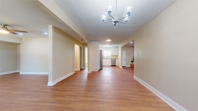 hallway with a textured ceiling, light wood finished floors, an inviting chandelier, and baseboards