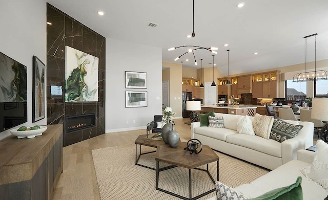 living area with a notable chandelier, recessed lighting, visible vents, light wood-style flooring, and a tiled fireplace