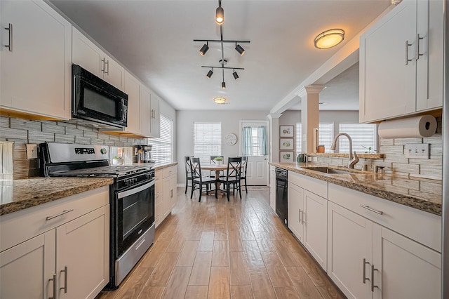 kitchen with stainless steel gas range, light wood-type flooring, ornate columns, black microwave, and a sink