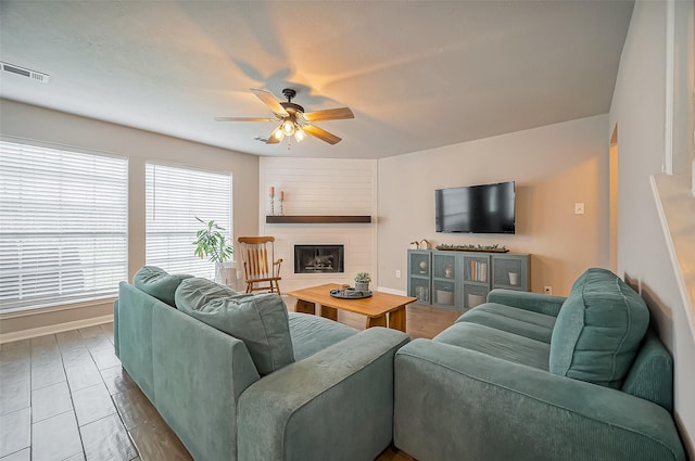 living area with a ceiling fan, visible vents, a fireplace, and baseboards