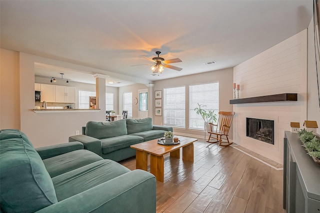 living area featuring a large fireplace, wood finished floors, visible vents, ornate columns, and track lighting