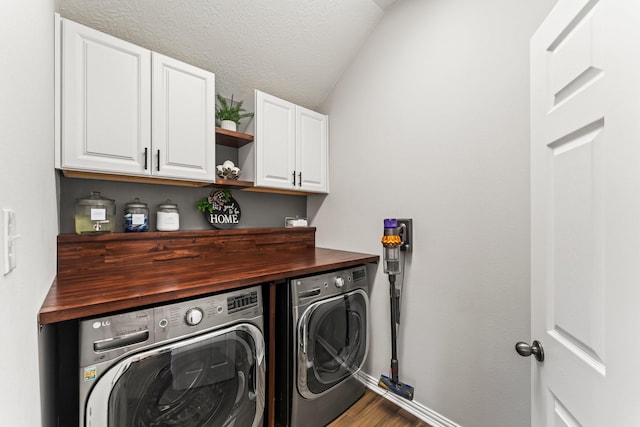 clothes washing area featuring a textured ceiling, wood finished floors, cabinet space, baseboards, and washing machine and clothes dryer