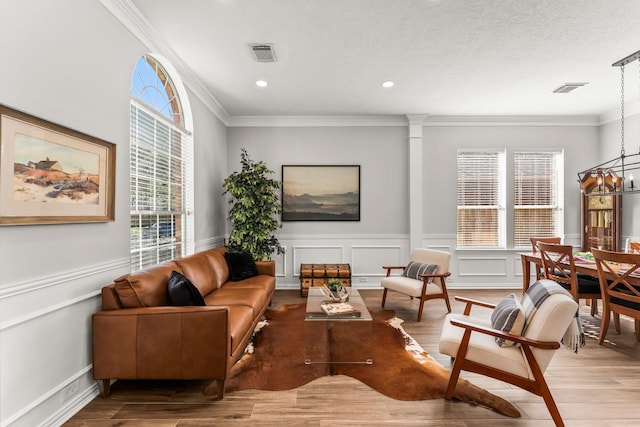 living room with visible vents, a textured ceiling, wood finished floors, and crown molding