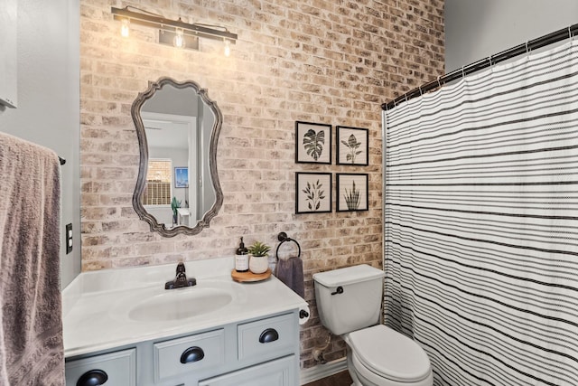 full bath with toilet, brick wall, and vanity