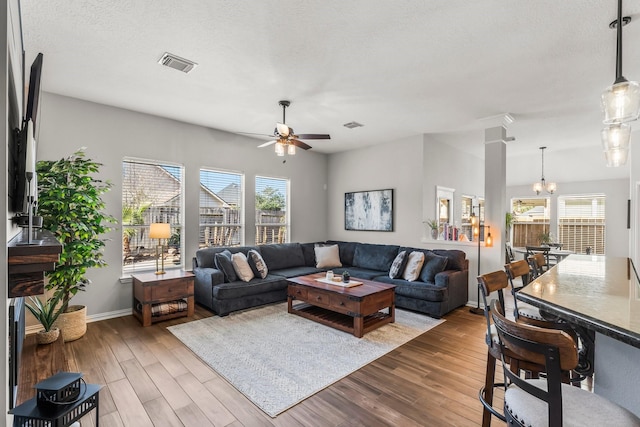 living area with ceiling fan with notable chandelier, wood finished floors, visible vents, and a textured ceiling