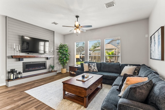 living room featuring visible vents, a fireplace, baseboards, and wood finished floors