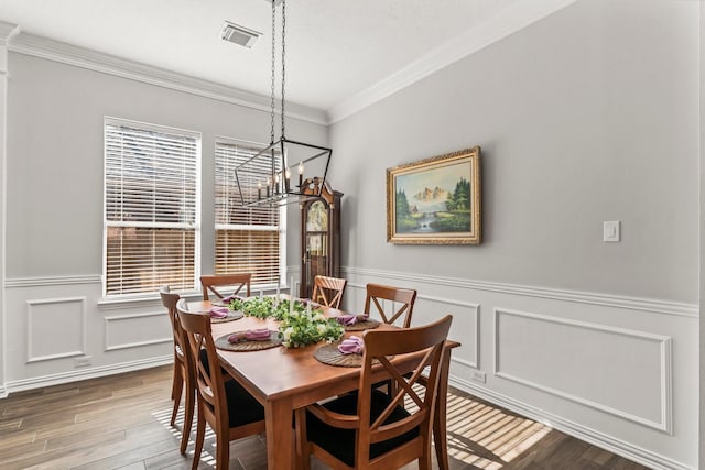 dining space featuring visible vents, ornamental molding, wainscoting, wood finished floors, and a notable chandelier