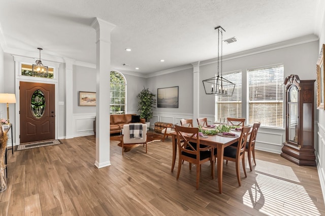 dining room featuring a textured ceiling, wood finished floors, ornate columns, and a chandelier