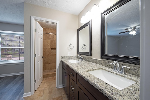 full bath with a tile shower, a textured ceiling, baseboards, and a sink