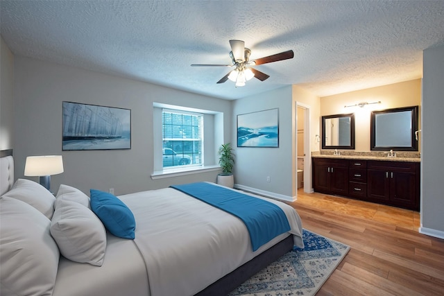 bedroom with a textured ceiling, ensuite bath, light wood-type flooring, and a sink