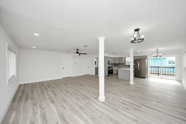 unfurnished living room featuring baseboards, ornate columns, a textured ceiling, light wood-style floors, and ceiling fan with notable chandelier