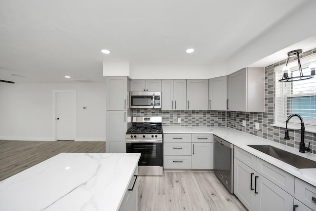 kitchen featuring stainless steel appliances, a sink, light stone counters, and gray cabinetry