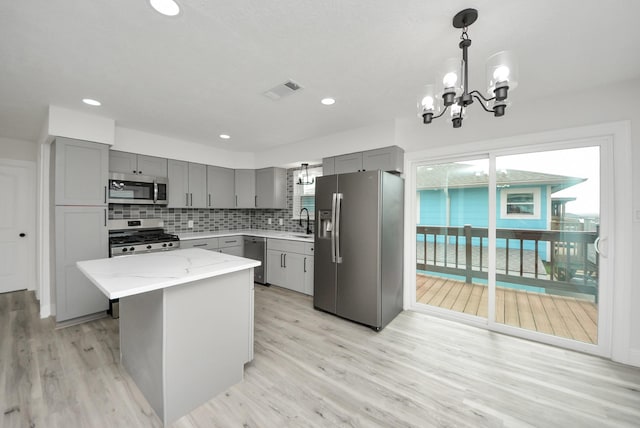 kitchen featuring light stone counters, gray cabinets, decorative backsplash, appliances with stainless steel finishes, and a sink