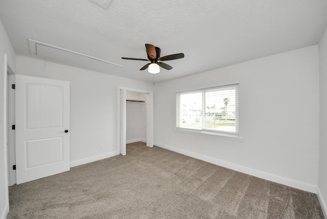 unfurnished bedroom with a closet, attic access, carpet flooring, a textured ceiling, and baseboards