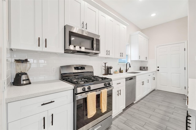 kitchen with a sink, white cabinetry, light wood-style floors, appliances with stainless steel finishes, and tasteful backsplash