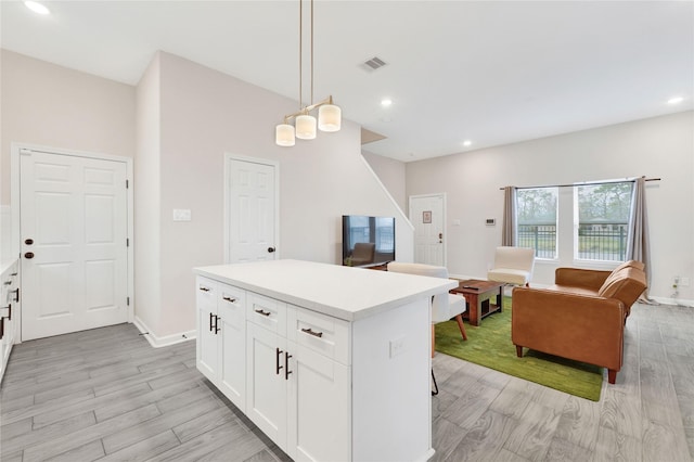 kitchen with light wood finished floors, visible vents, white cabinets, and a center island