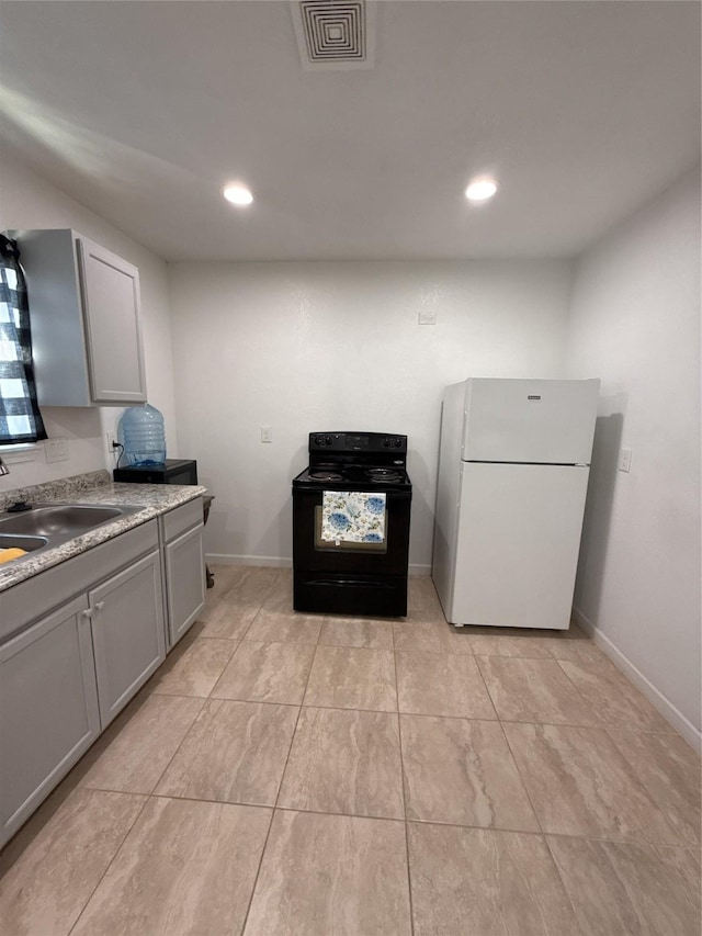 kitchen featuring visible vents, gray cabinetry, freestanding refrigerator, a sink, and black / electric stove