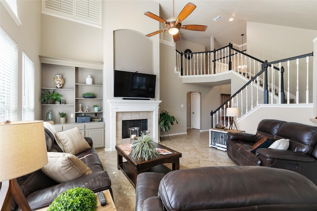 living area with stairway, a tiled fireplace, high vaulted ceiling, ceiling fan, and visible vents
