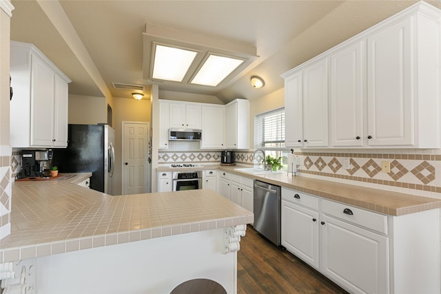 kitchen with a sink, stainless steel appliances, decorative backsplash, a peninsula, and white cabinets