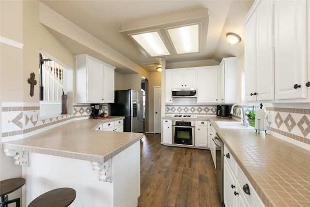 kitchen with stainless steel appliances, a peninsula, a sink, white cabinets, and dark wood-style floors