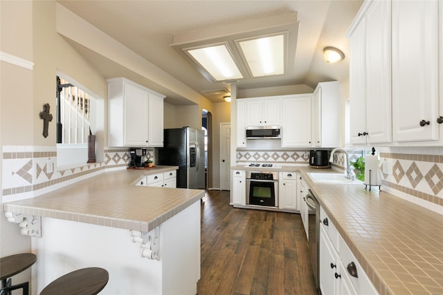 kitchen featuring a sink, decorative backsplash, a peninsula, white cabinetry, and appliances with stainless steel finishes