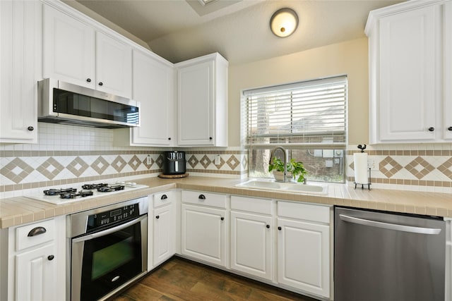 kitchen with appliances with stainless steel finishes, dark wood-type flooring, a sink, white cabinetry, and backsplash