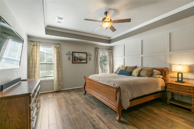 bedroom with a tray ceiling, visible vents, a decorative wall, a textured ceiling, and wood finished floors